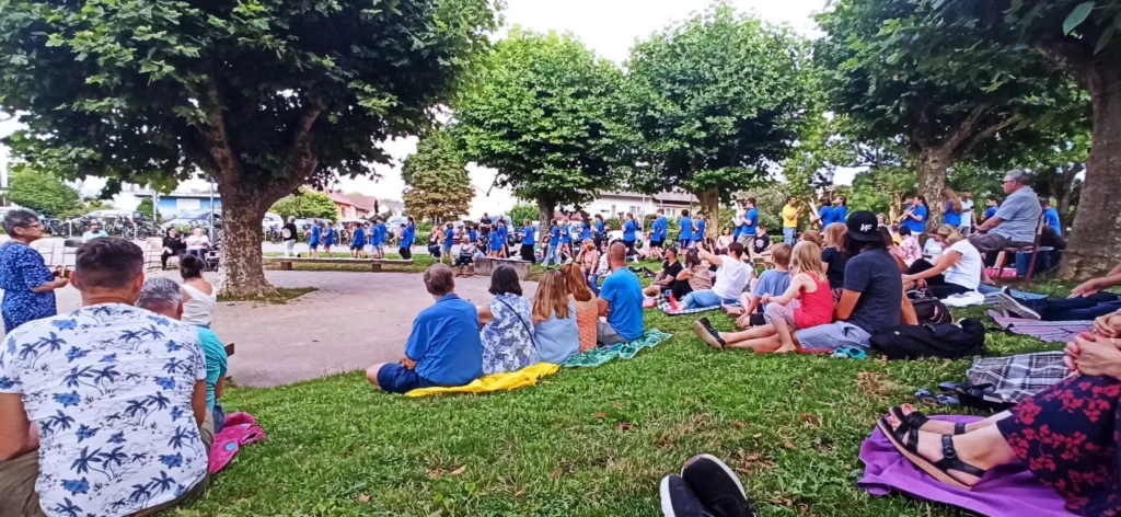 Personen sitzen beim Bläserpicknick auf der Wiese des Schulhofs. 