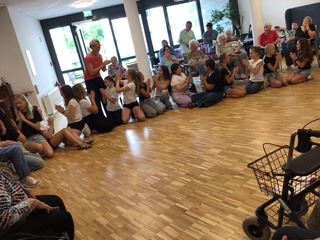 uf dem Foto sitzen Schüler und Bewohner des Altenheims im Kreis und spielen ein Klatschspiel